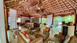 A spacious lounge area with wicker furniture, a thatched roof, and a view of lush greenery. - Piedra de Agua Hotel Boutique Palenque (Palenque)