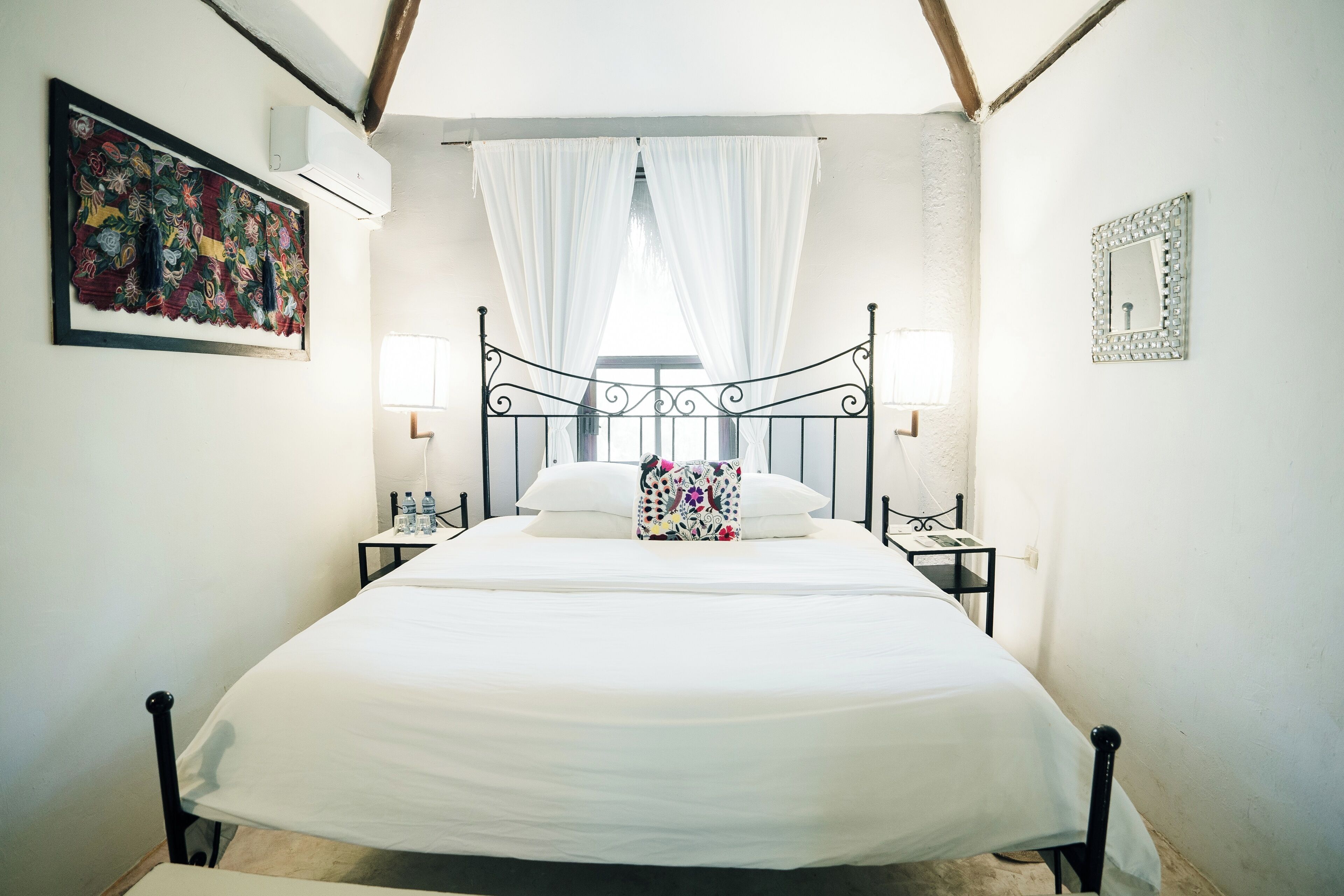 A neatly made bed with white linens, a decorative pillow, and a bedside table with a lamp.