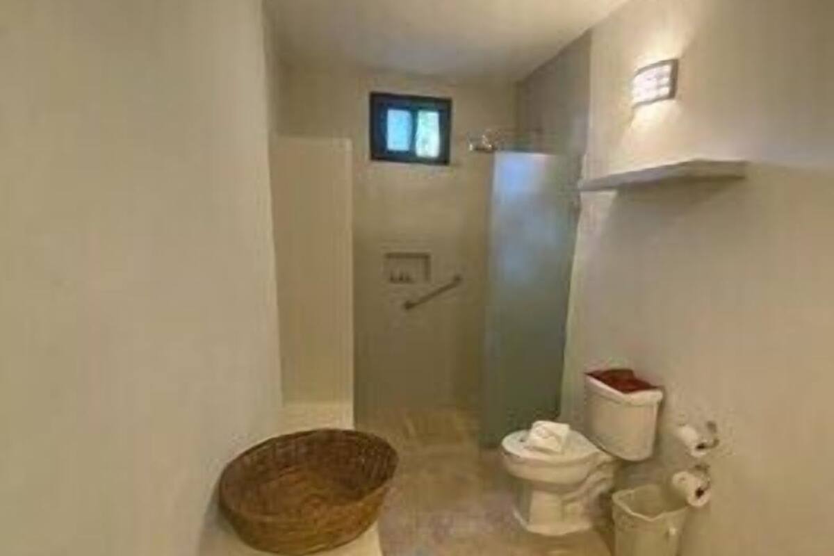 Ein schmales Badezimmer mit Toilette, einem kleinen Fenster und einem an der Wand befestigten Regal.