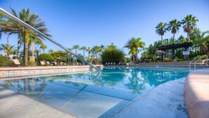Una piscina cristalina con sillas de descanso y palmeras al fondo.