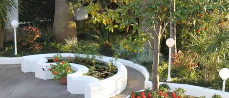 A landscaped garden with white curbs, a pond, and red flowers.