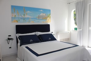 Ein Hotelzimmer mit einem Bett, einem Meeresblick Gemälde, einem Fenster mit Vorhängen und einem Thermostat an der Wand.