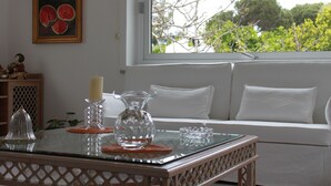 A room with a glass table, white sofa, and a window with a view of trees.
