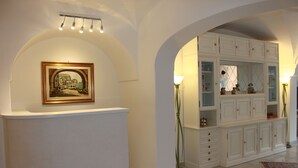A hallway with a white archway, a framed painting, a cabinet with glass doors, and a floor lamp.