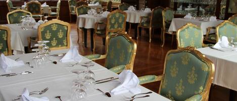 Un comedor formal con varias mesas dispuestas para el servicio, cada una con sillas tapizadas en verde y manteles blancos.