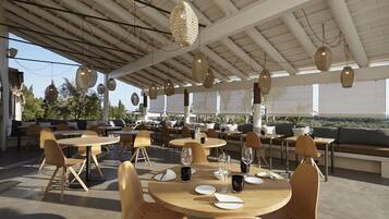 An outdoor dining area with round tables and chairs, hanging wicker lamps, and a view of the landscape.
