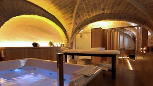 Un cuarto de spa con una bañera grande, bancos de madera y un techo abovedado de ladrillo.