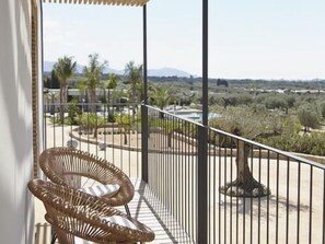 A balcony with wicker chairs, a view of a landscaped area with trees and shrubs, and a distant mountain range. - Hotel Mas Lazuli (Pau)