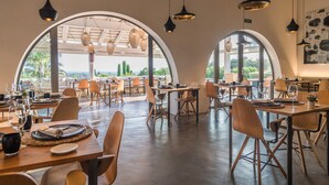 Un amplio comedor con varias mesas y sillas, grandes ventanales en arco y luminarias colgantes.