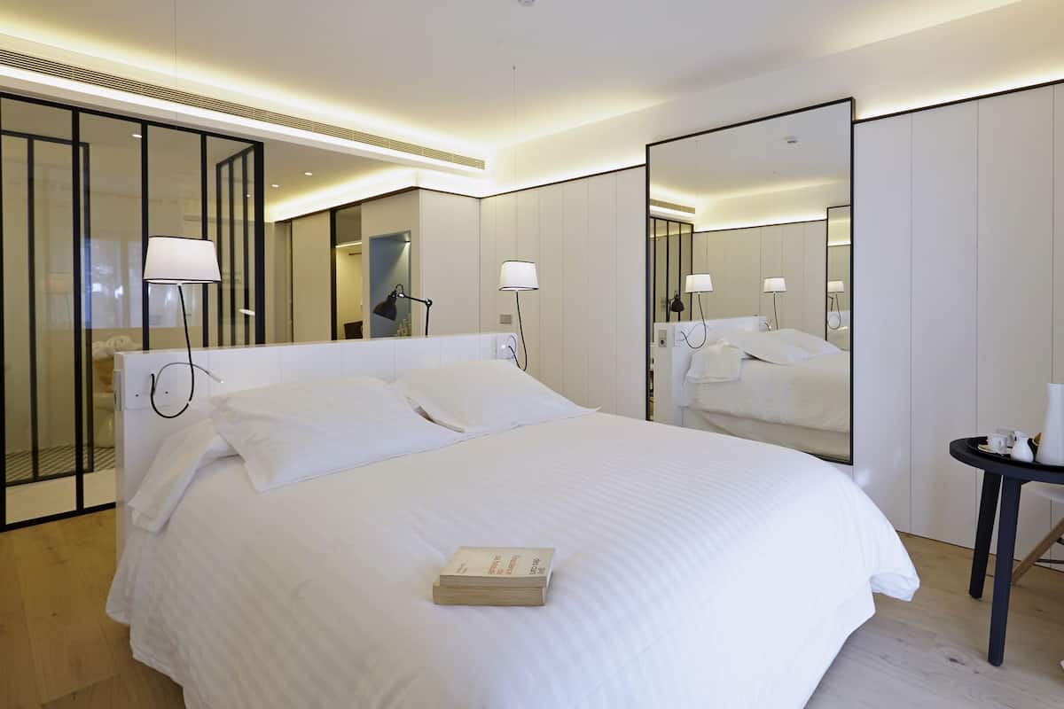 Une chambre d’hôtel moderne avec un grand lit, des lampes de chevet, un miroir et une petite table sur laquelle est posé un vase.