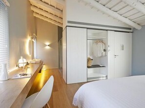A modern hotel room with a wooden desk, a large bed, a wardrobe, and a mirror.
