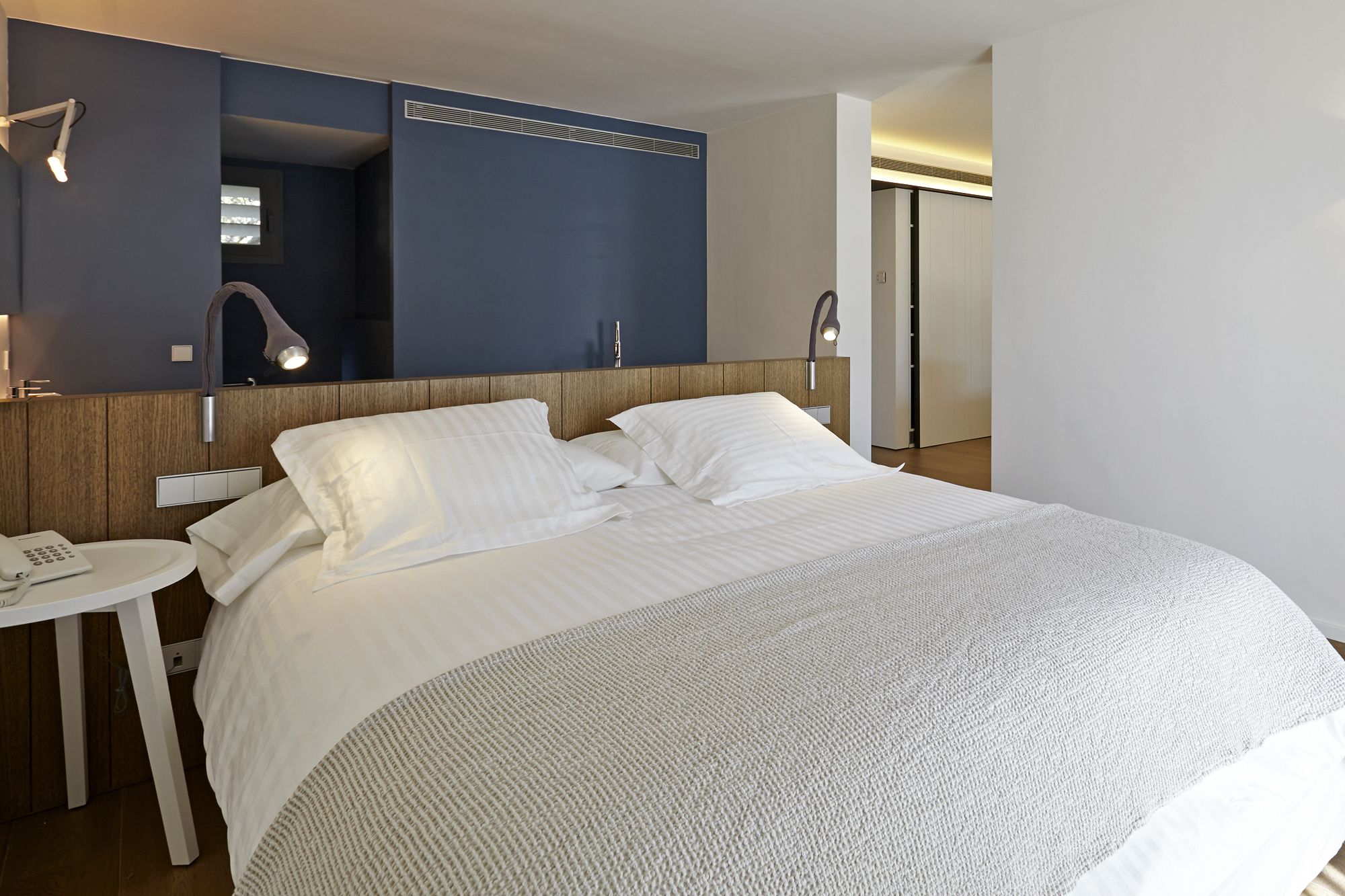 Habitación de hotel con una cama grande, una mesita de noche con teléfono, un espejo y un calentador de pared.