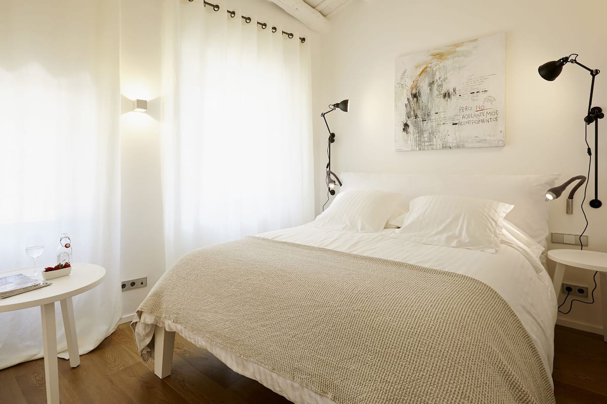 Une chambre à coucher bien rangée, avec un lit, des tables de chevet, une petite table sur laquelle se trouve un verre d’eau, et un tableau accroché au mur.