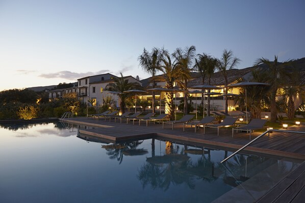A poolside area with lounge chairs and umbrellas, surrounded by palm trees and buildings. - Hotel Mas Lazuli (Pau)