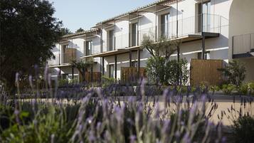 Un edificio residencial moderno con varios balcones, un patio con plantas de lavanda y una cerca de madera.
