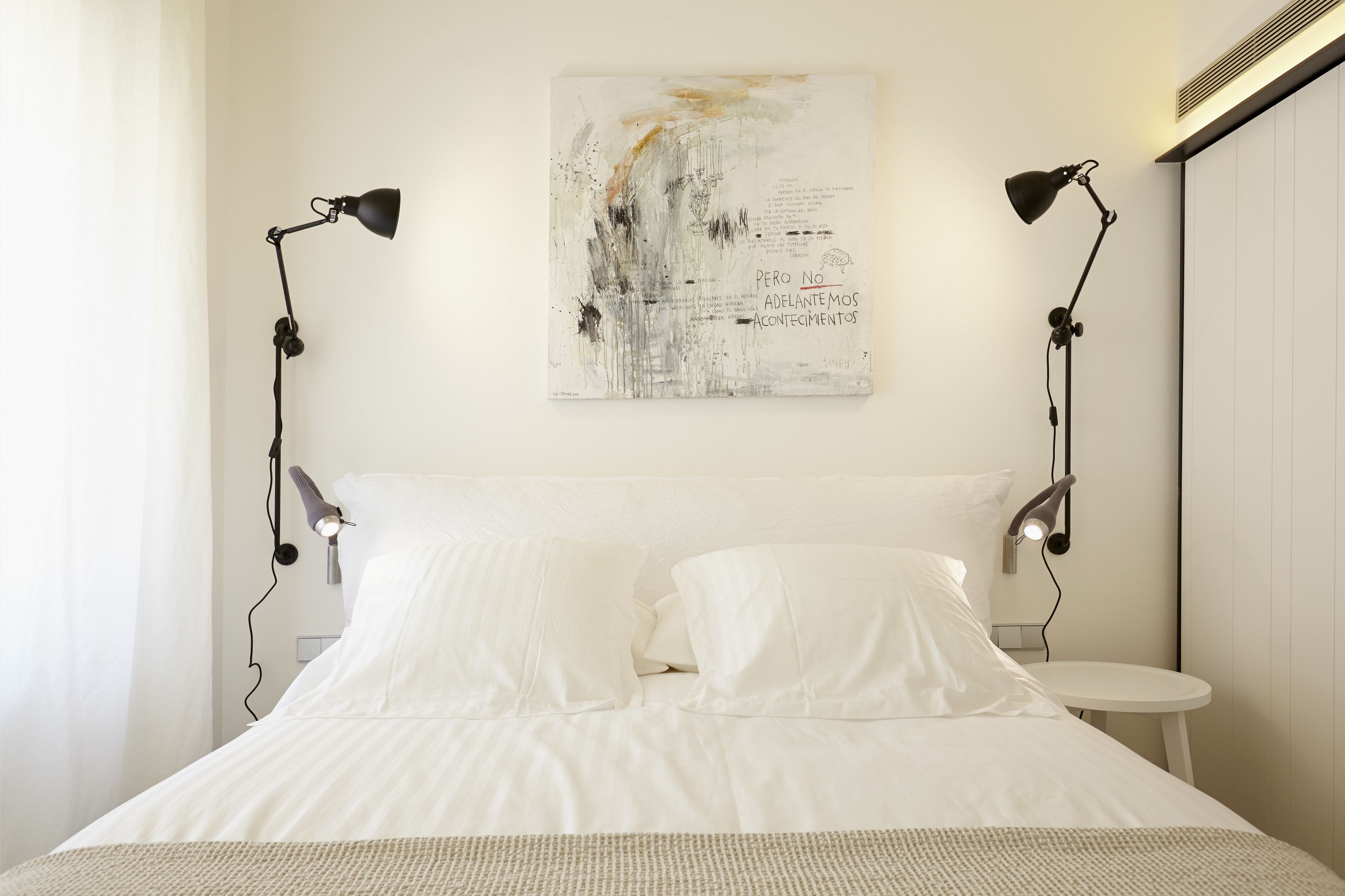 A modern bedroom with a large bed, two bedside lamps, and a wall-mounted abstract painting.