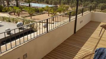 Un balcón con piso de madera, baranda de metal y vista a una piscina y follaje.