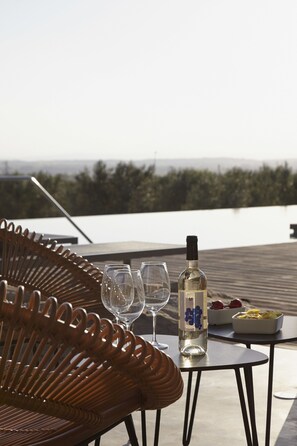 A wicker chair, two wine glasses, a bottle of white wine, and a bowl of fruit on a small table with a view of a forested landscape. - Hotel Mas Lazuli (Pau)