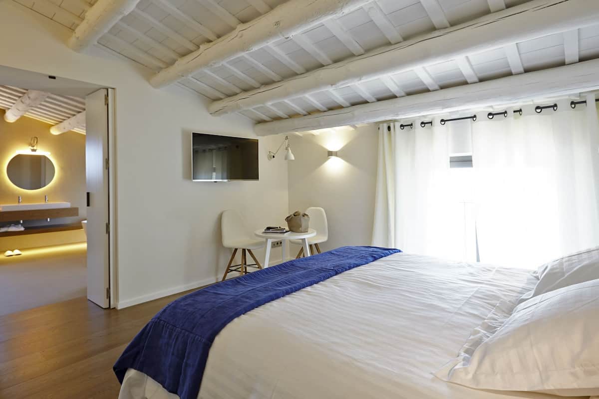 Une chambre avec un grand lit, un bureau avec une chaise, une télévision et une salle de bain avec un miroir et un lavabo.