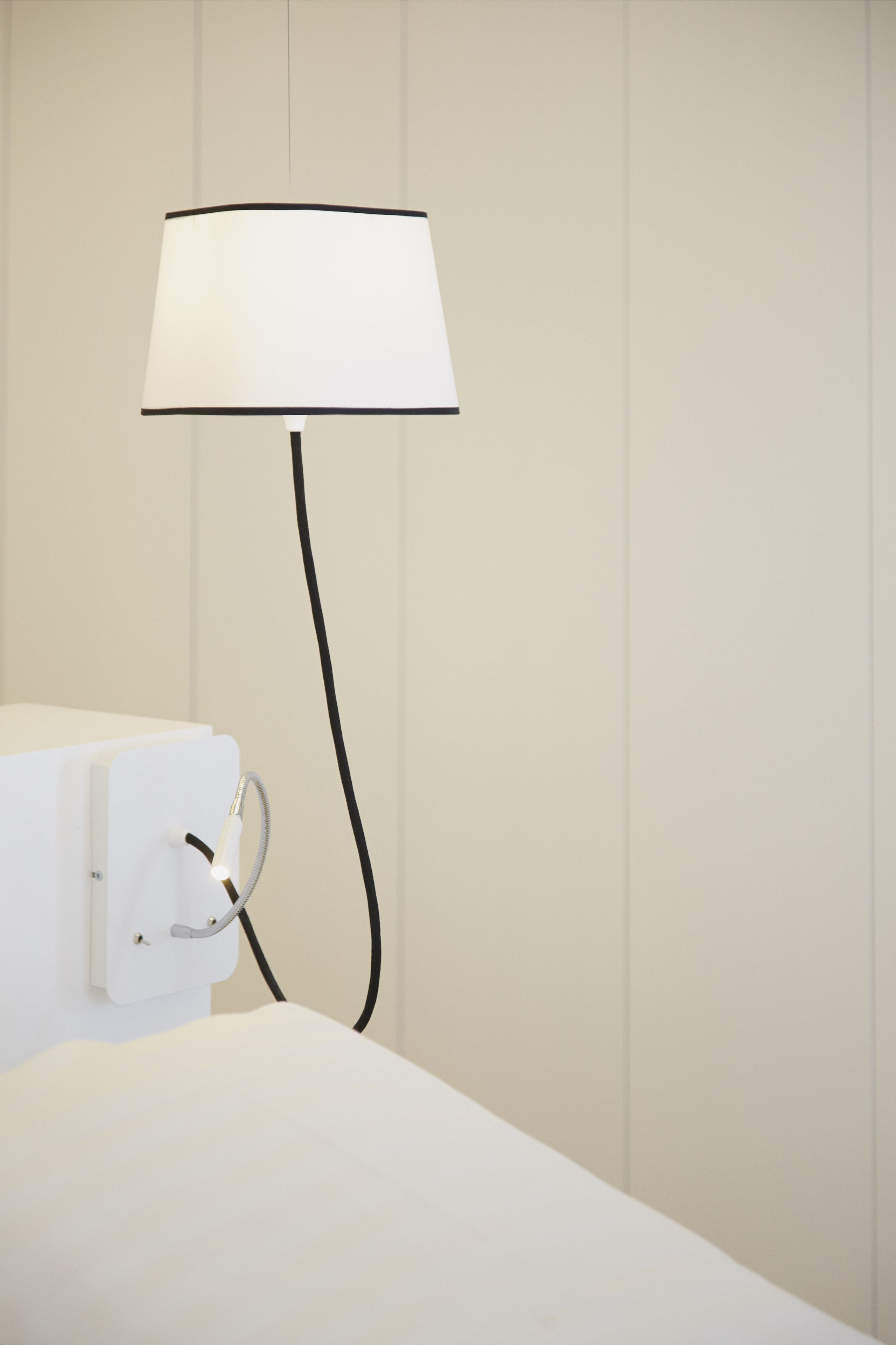 Een nachtkastje, wit van kleur, met een lamp en een stopcontact.
