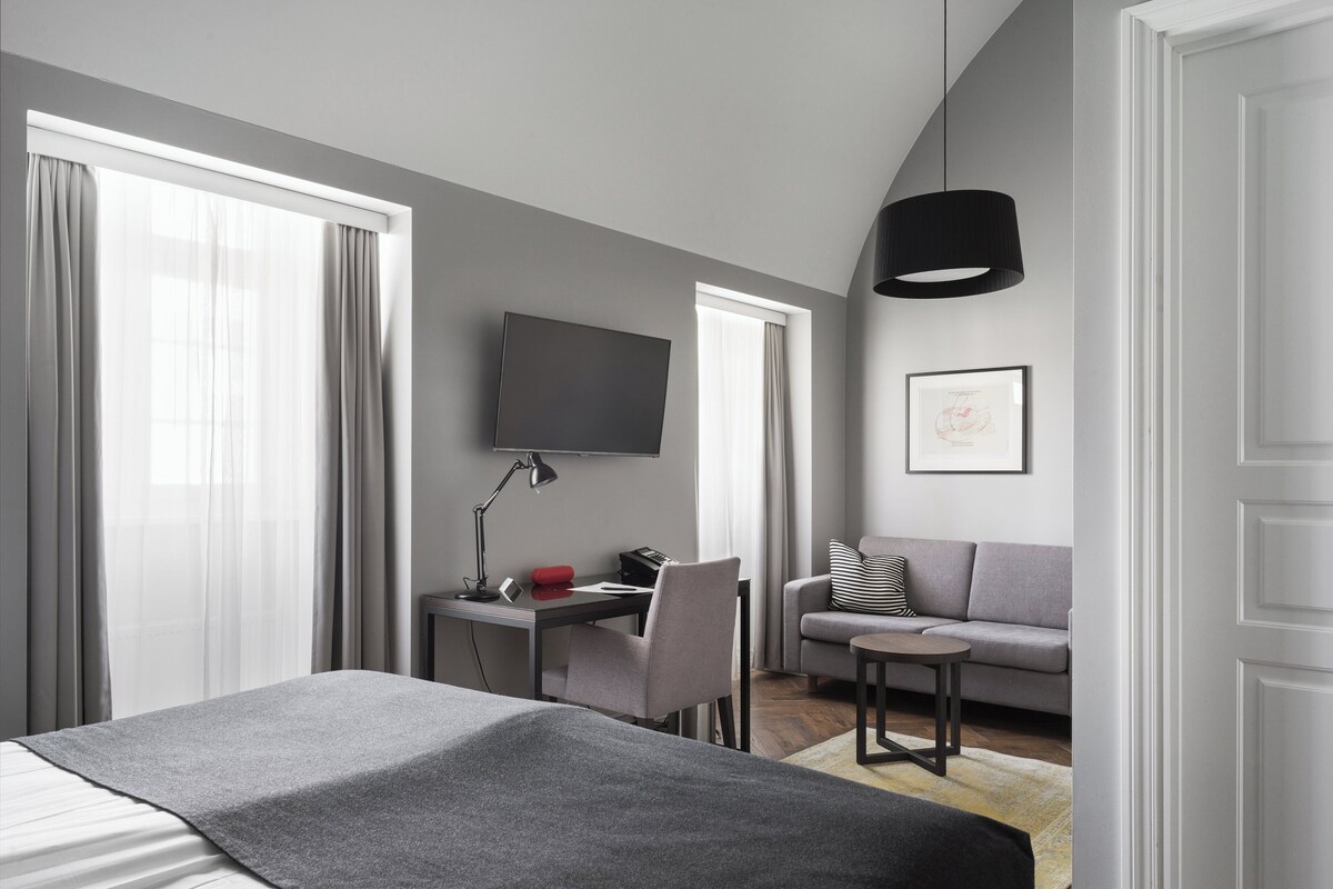 Ett modernt hotellrum med en säng, ett skrivbord med en dator, en soffa och en tv som är monterad på väggen.