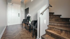 A hallway with a wooden floor, a white door, a staircase with wooden steps, and two chairs with a potted plant. - Apotek Hotel by Keahotels (Reykjavik)