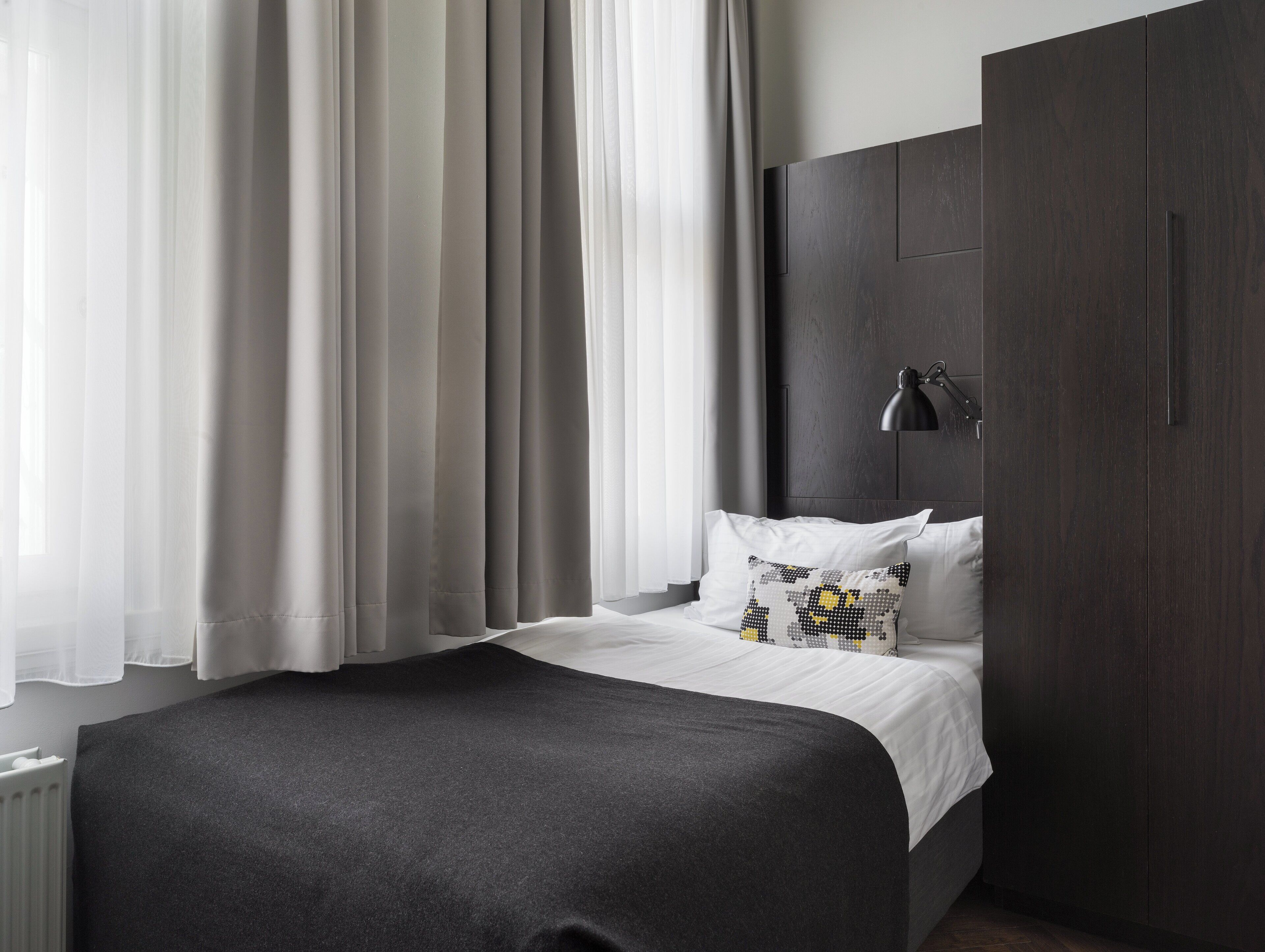 A modern bedroom with a large bed, dark wood wardrobe, and sheer curtains.