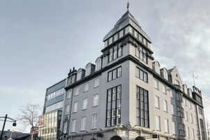 Un edificio storico con una torre d'angolo imponente, ampie finestre e una facciata simmetrica.