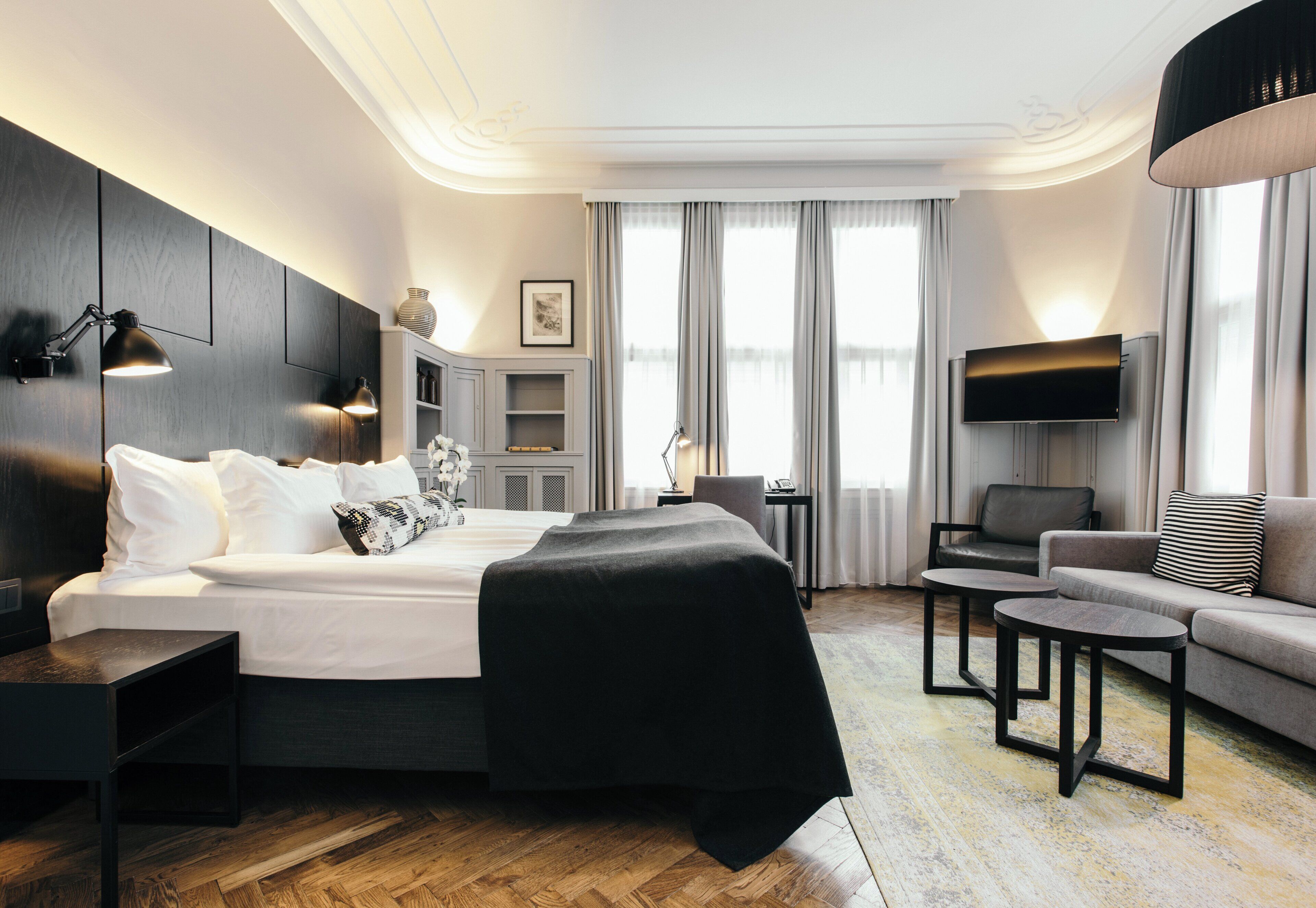 A modern hotel room with a large bed, a sofa, a TV, and a desk.
