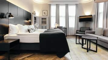 A modern hotel room with a large bed, a sofa, a TV, and a desk.