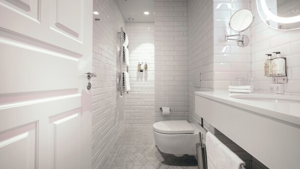 Ein modernes Badezimmer mit weißen Fliesen, einer Toilette, einem Waschbecken mit Spiegel und einer Duschkabine.