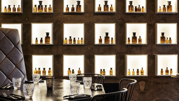 Un espace repas avec un mur en bois, plusieurs étagères éclairées où sont exposées des bouteilles, un fauteuil en cuir foncé et un plancher en bois.