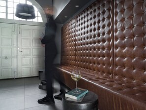 En person går förbi en brun lädersoffa. På ett runt bord står en bok och ett glas vin.