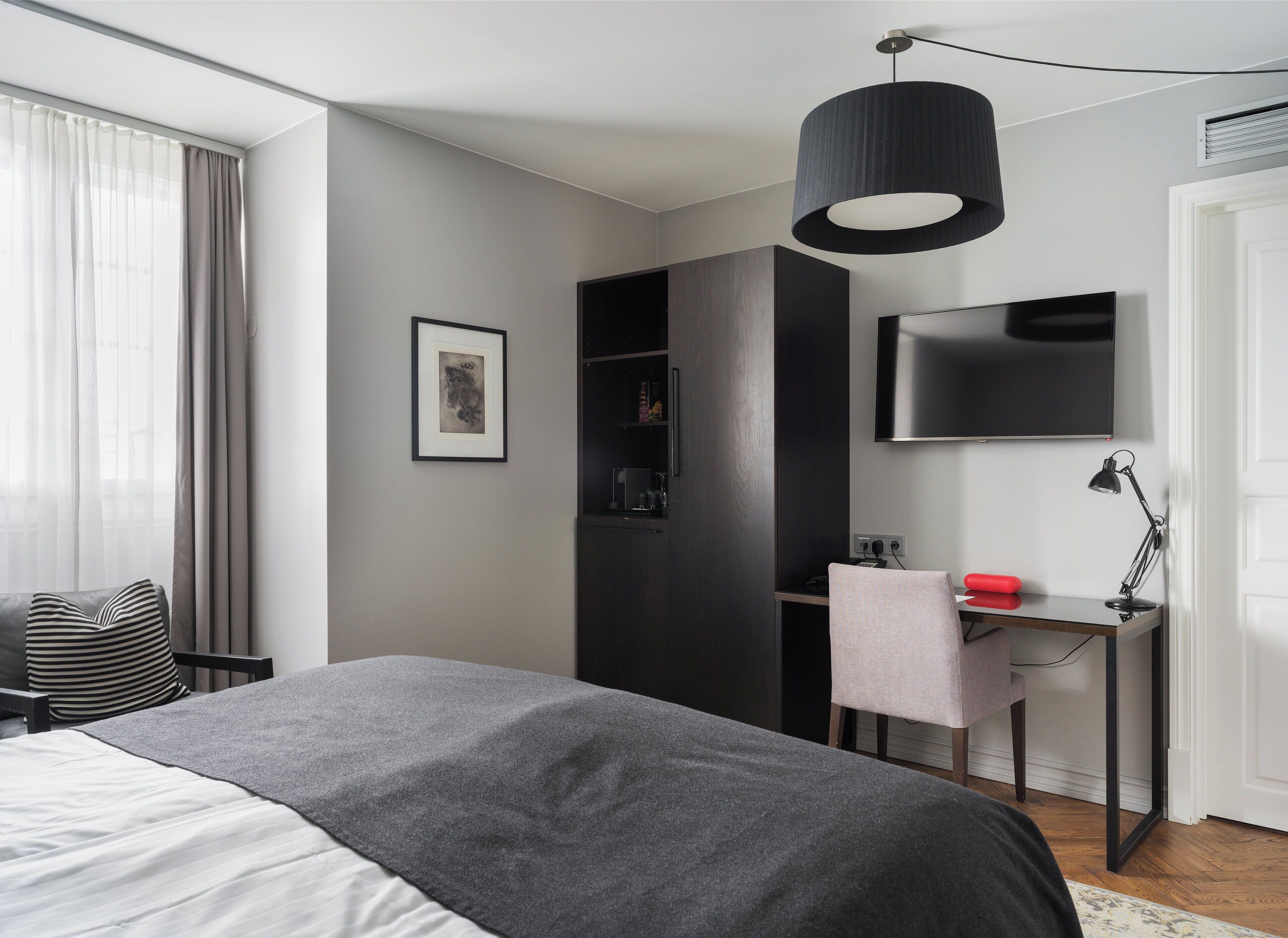 Ein modernes Schlafzimmer mit einem großen Bett, einem Schreibtisch mit Stuhl, einem an der Wand montierten Fernseher und einem Kleiderschrank.