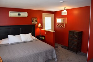 A bedroom with a bed, a nightstand, a lamp, a dresser, and a window with blinds.