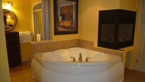 A bathroom with a large oval bathtub, a mirror, a framed picture on the wall, and a television mounted on the wall.