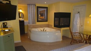 A hotel room with a large bathtub, a bed, a small table, and a chair.