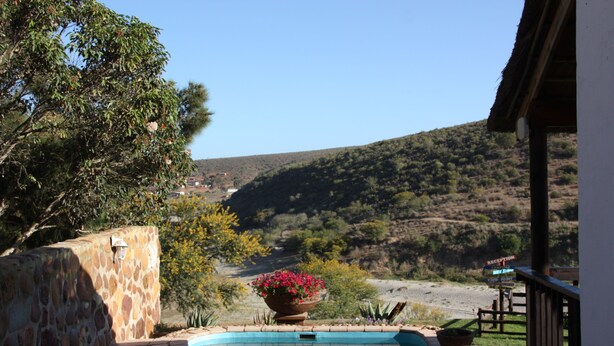 A pool area with a stone wall, a reception sign, and a view of a hilly landscape. - Gourits River Guest Farm (Albertinia)