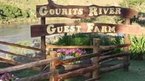 A wooden sign with the text "Gourits River Guest Farm" in a rustic setting with a river and greenery in the background. - Gourits River Guest Farm (Albertinia)
