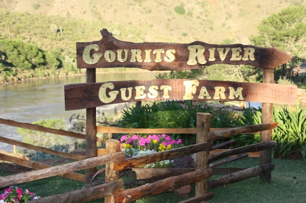 A wooden sign with the text "Gourits River Guest Farm" in a rustic setting with a river and greenery in the background.