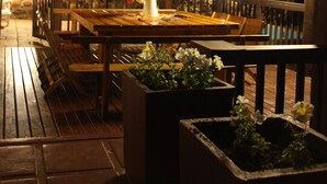 An outdoor wooden deck with a table and chairs, surrounded by planters with flowers. - Gourits River Guest Farm (Albertinia)