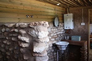 A rustic bathroom with a stone wall, wooden ceiling, a sink, and a mirror.