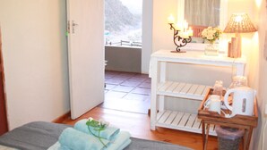 A room with a bed, a table with a lamp, a mirror, and a view of a mountainous landscape. - Gourits River Guest Farm (Albertinia)