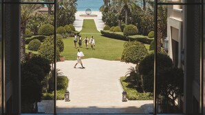 A view through an arched window of a well-maintained garden with a pathway leading to a beach. - Four Seasons Resort Dubai at Jumeirah Beach (Dubai)