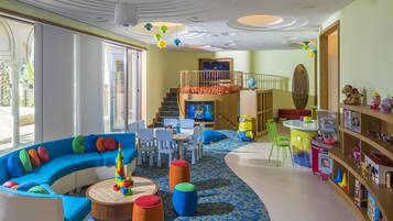 Children can play and learn in this vibrant playroom with a sofa, table, chairs, bookshelf, and play kitchen set.