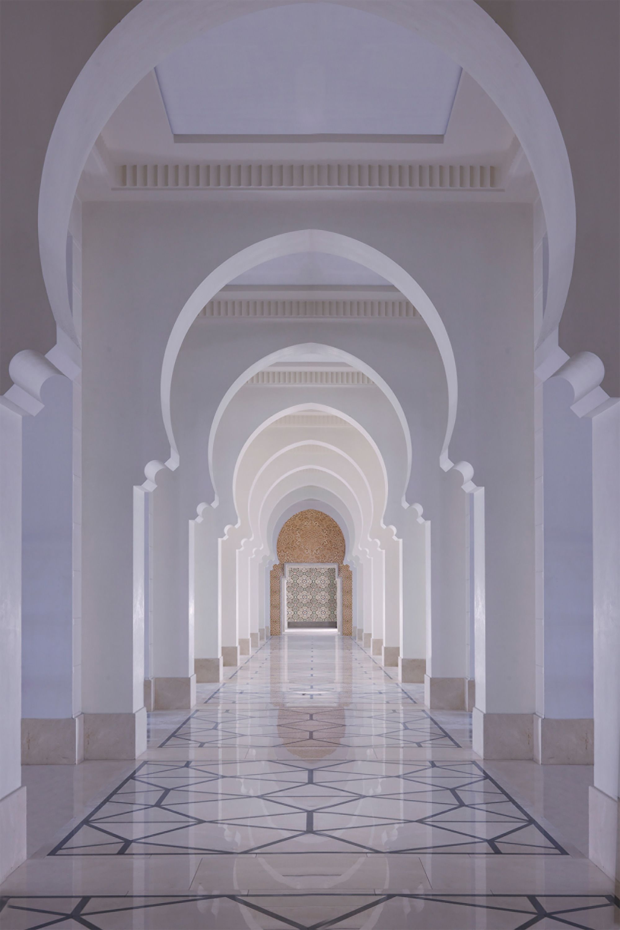A corridor with arches and a patterned floor, leading to a room with a patterned wall.