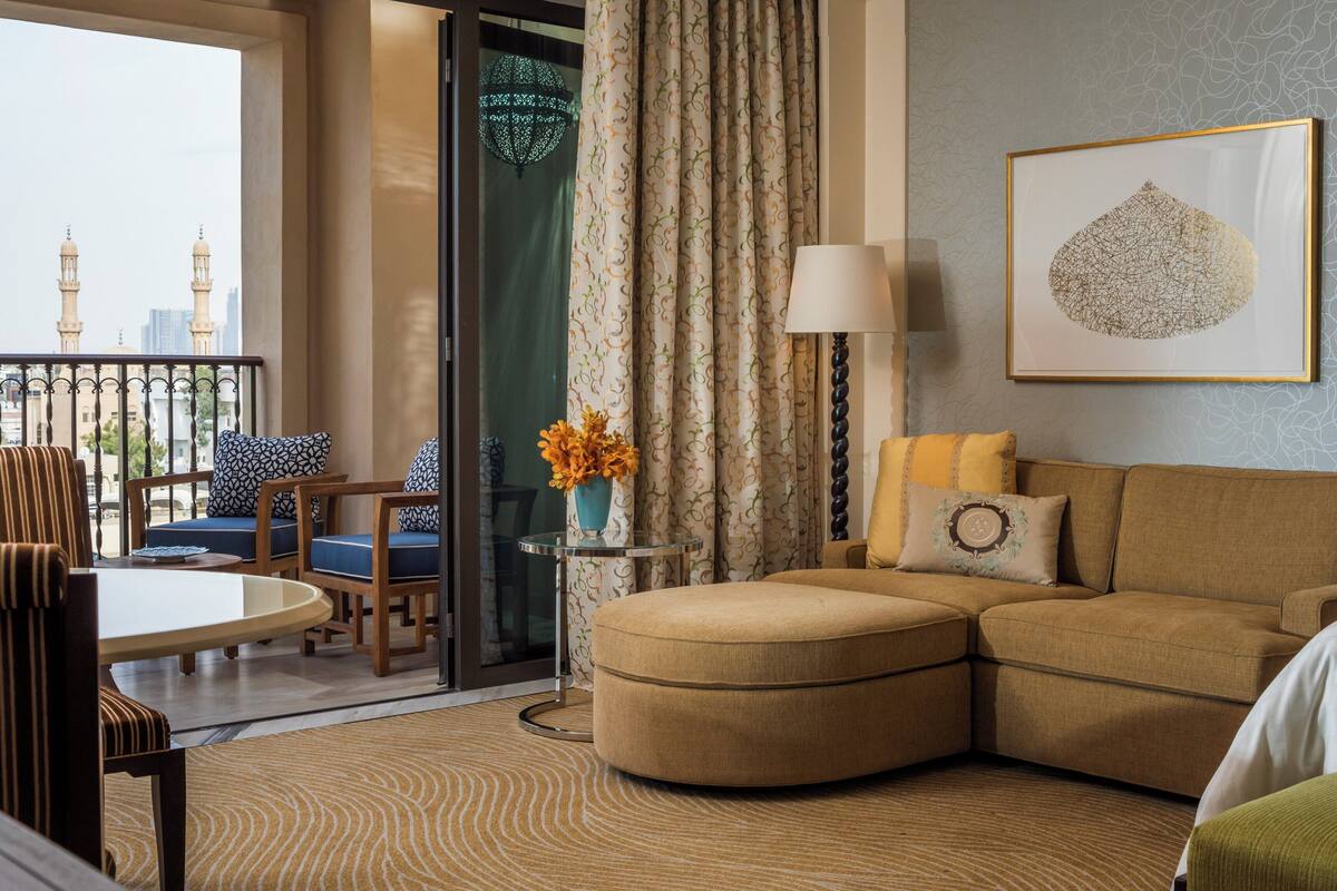 A hotel room with a balcony, a sofa, a table, and a lamp.