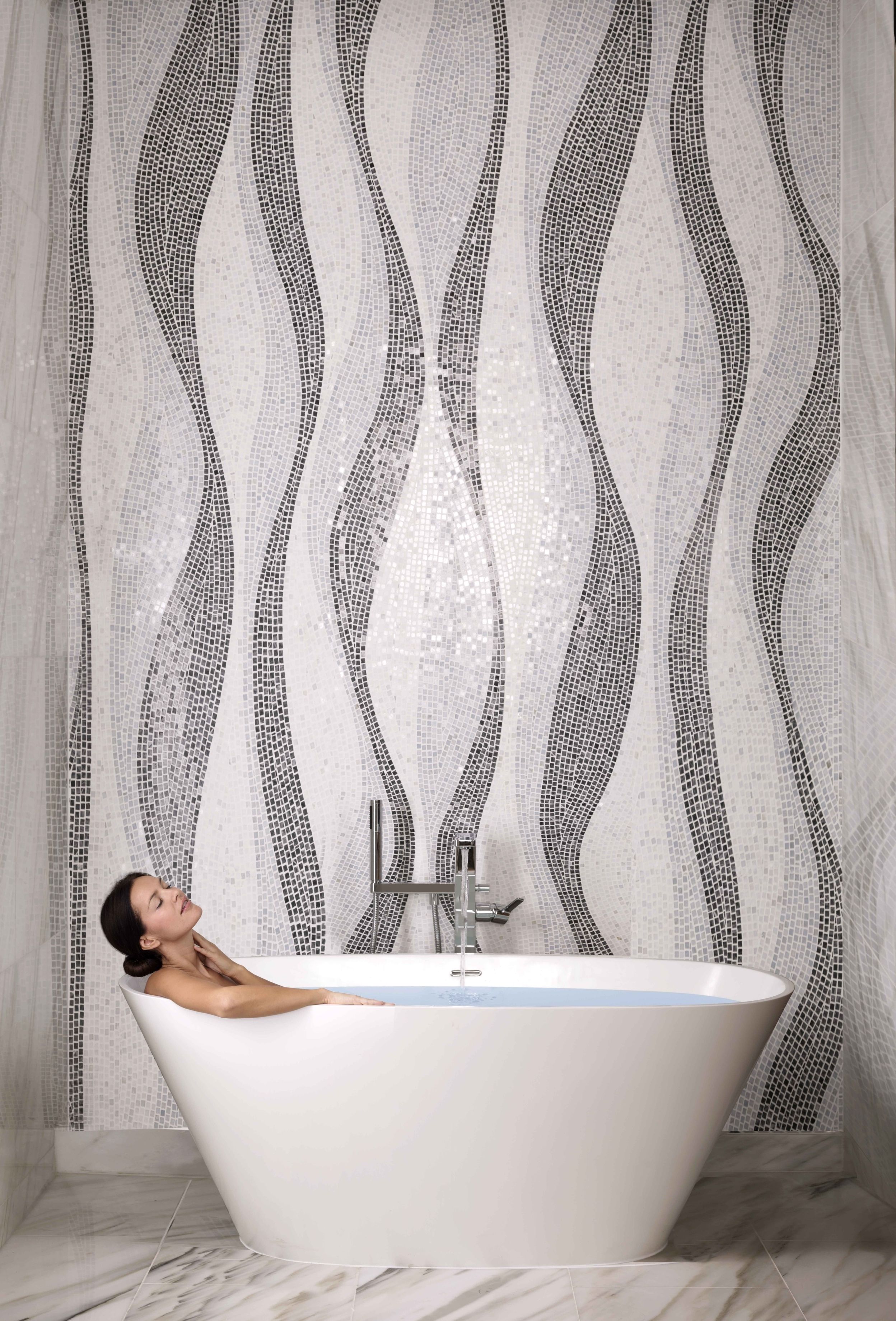A bathtub in a bathroom with a tiled wall featuring a wavy pattern.