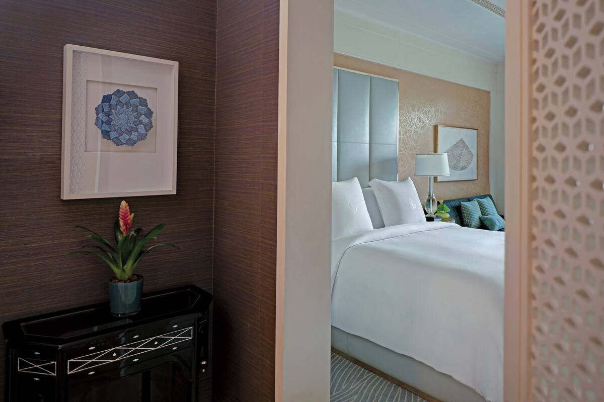 A hotel room with a bed, a nightstand, a potted plant, and a framed artwork on the wall.