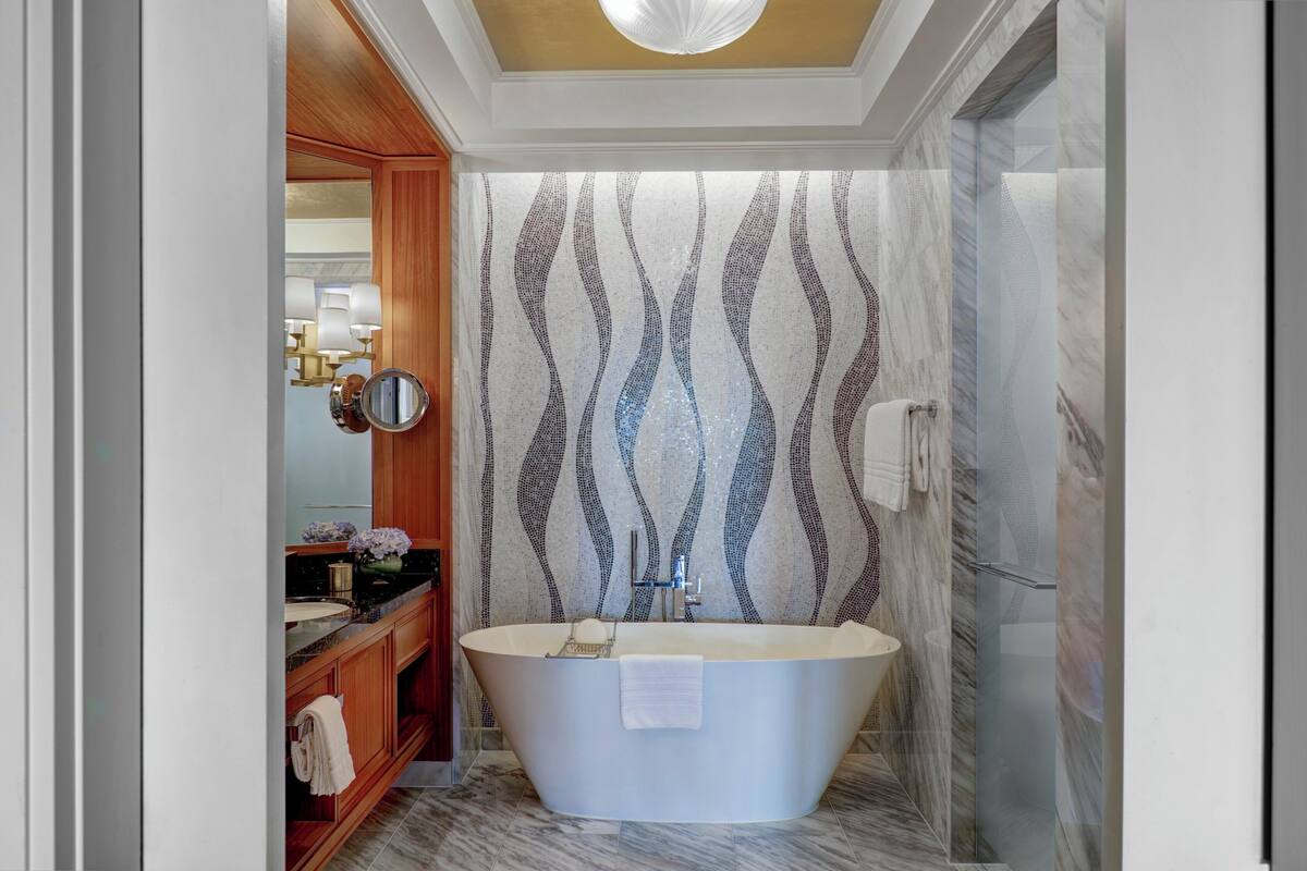 A modern bathroom with a freestanding bathtub, a vanity with a mirror, and a patterned wall.